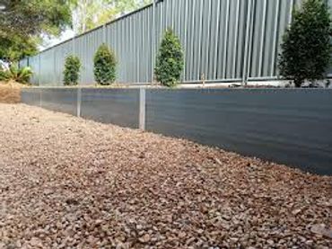 Gravel-covered ground with a grey retaining wall and neatly trimmed bushes.