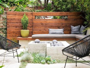 Modern outdoor seating area with wooden bench, black chairs, and green plants.