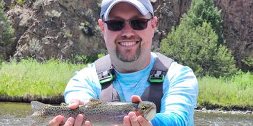 Man holding a freshly caught fish with a scenic outdoor background.