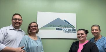Four smiling people standing in front of a chiropractic office sign.