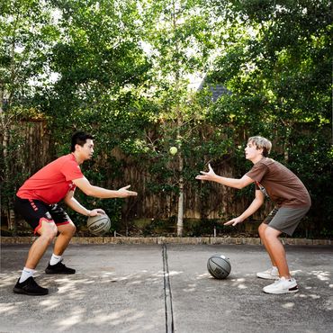 Two young men passing basketballs to each other on a driveway.
