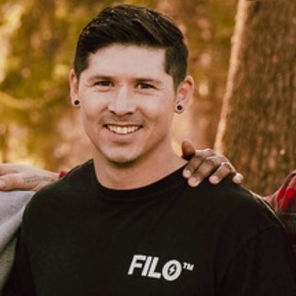 Smiling man with short hair and earrings outdoors.