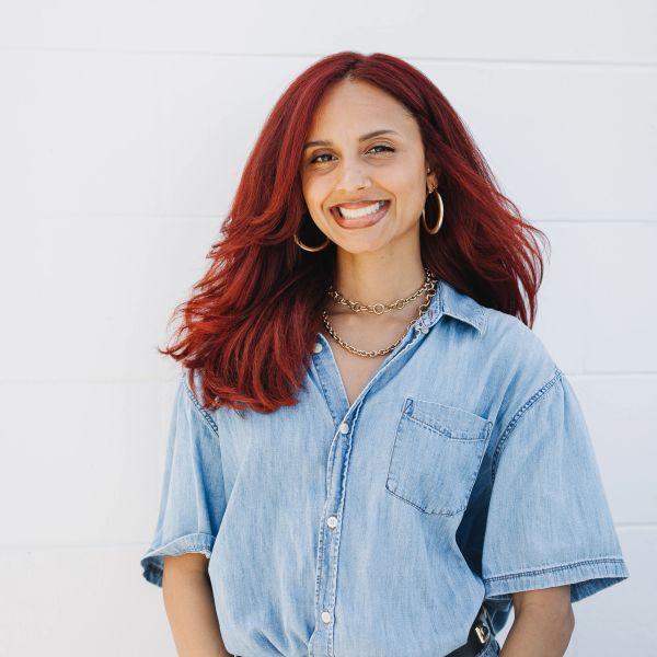 Smiling woman with vibrant red hair in a denim shirt.