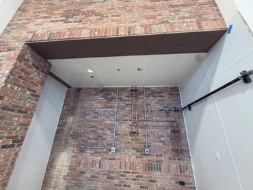 Exposed brick wall with electrical and plumbing pipes in an industrial-style interior.
