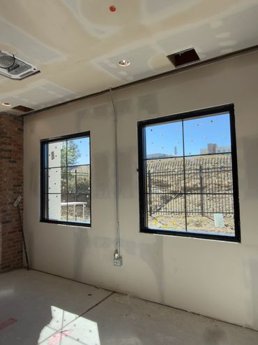 Room under construction with two taped windows and exposed brick.