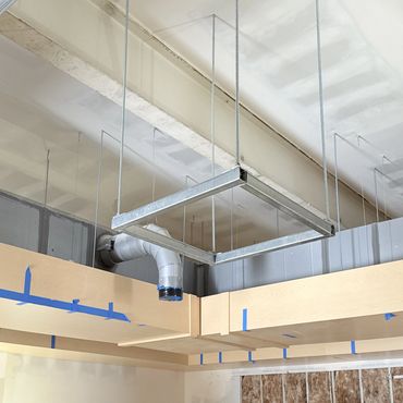 Exposed HVAC duct and metal frame suspended from ceiling in unfinished room.