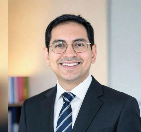 Professional man in suit smiling with glasses in office setting.