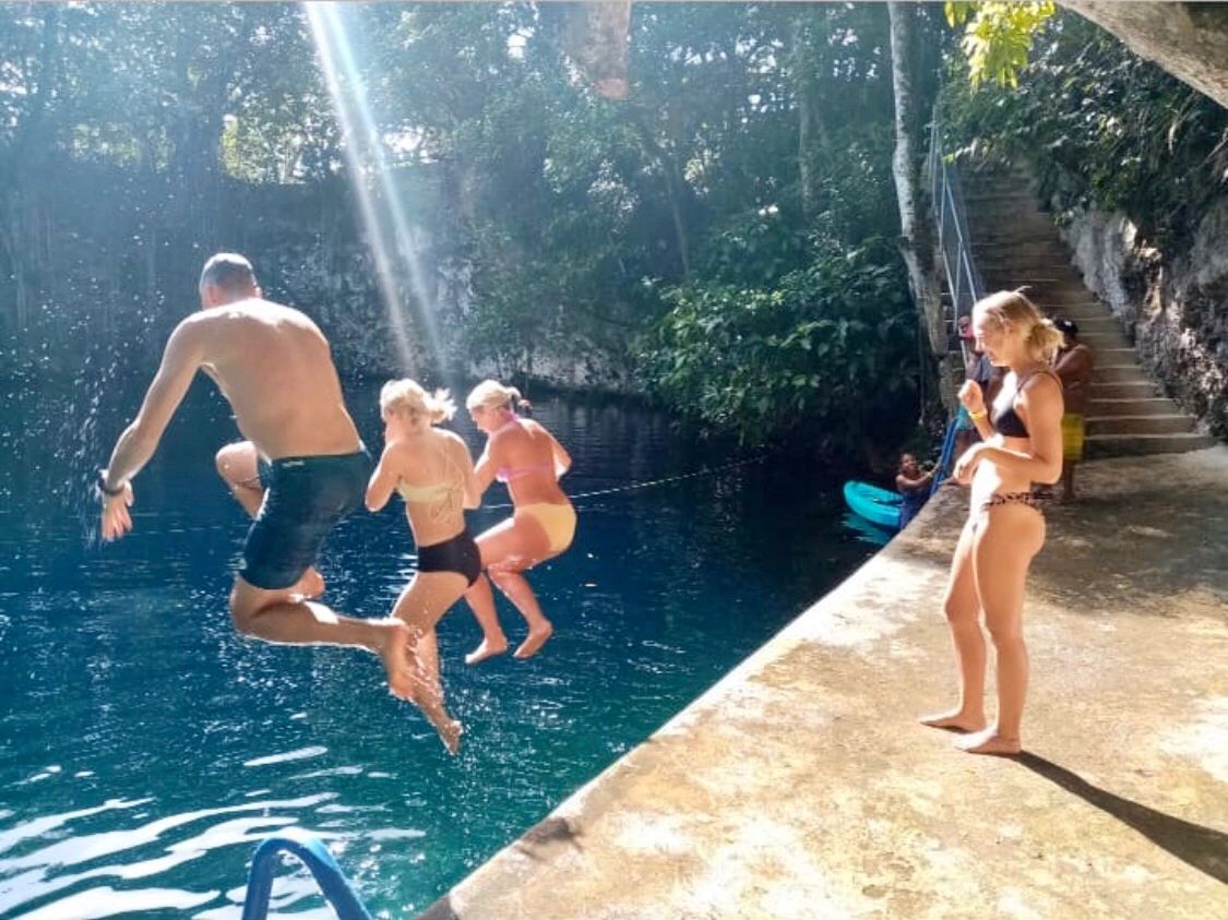 Group of people jumping into a natural pool surrounded by trees.