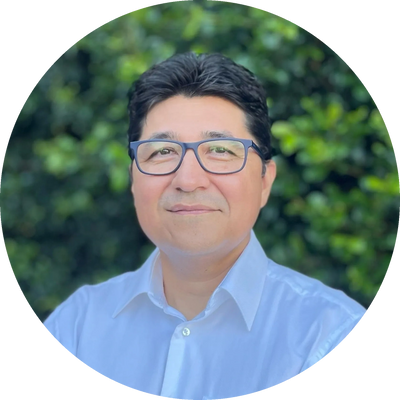 Jorge, mortgage broker in Australia, in white shirt and blue specs, with lush green backdrop.