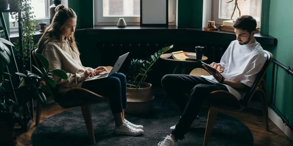 Two people working on laptops in a cozy, plant-filled room with green walls.