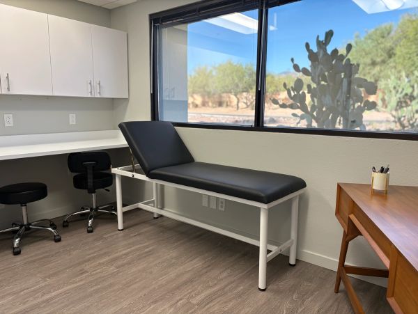A clean medical exam room with a black exam table and a wooden desk.