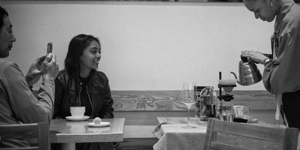 People enjoying coffee as a barista prepares a pour-over brew in a café.