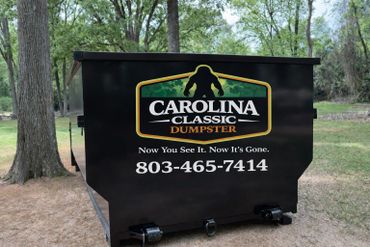 Black dumpster with Carolina Classic Dumpster logo and contact number in a park.
