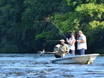 Three people fishing from a small boat on a river.