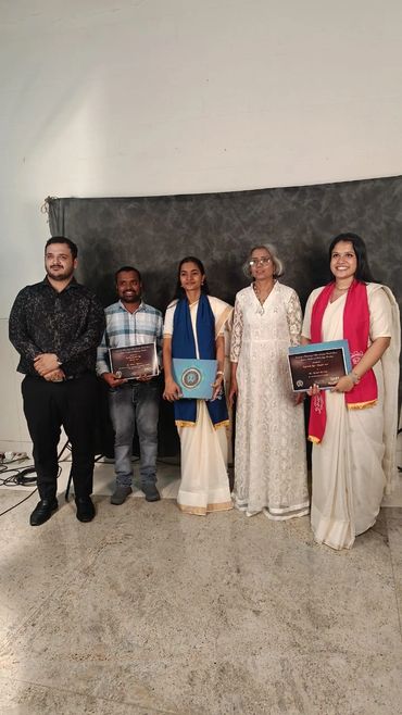 Five people standing against a backdrop, three holding certificates, dressed formally.