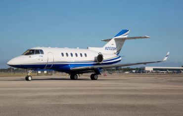 A sleek white and blue private jet parked on the runway under a clear sky.