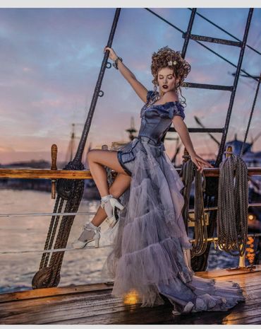 Woman in elegant dress posing on a ship at sunset.