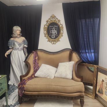 Vintage room with antique sofa, mannequin in lace dress, and ornate framed sign.