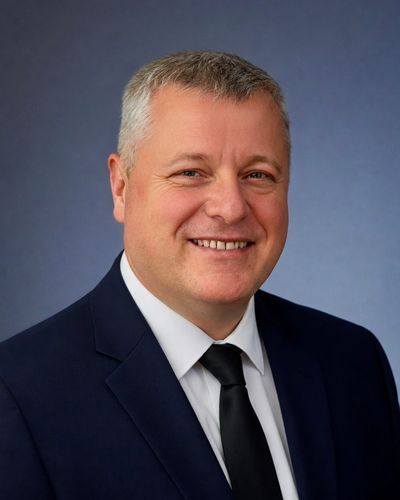Smiling middle-aged man in a dark suit and tie against a blue background.