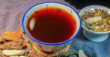 A cup of herbal tea surrounded by dried herbs and roots on a cloth.