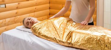 Woman wrapped in a golden thermal blanket during a spa treatment.