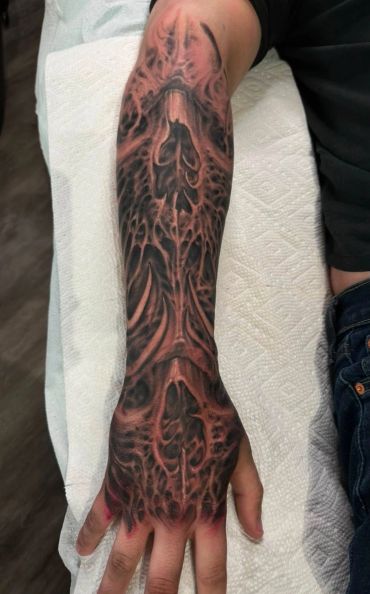Dark biomechanical tattoo covering forearm and hand.