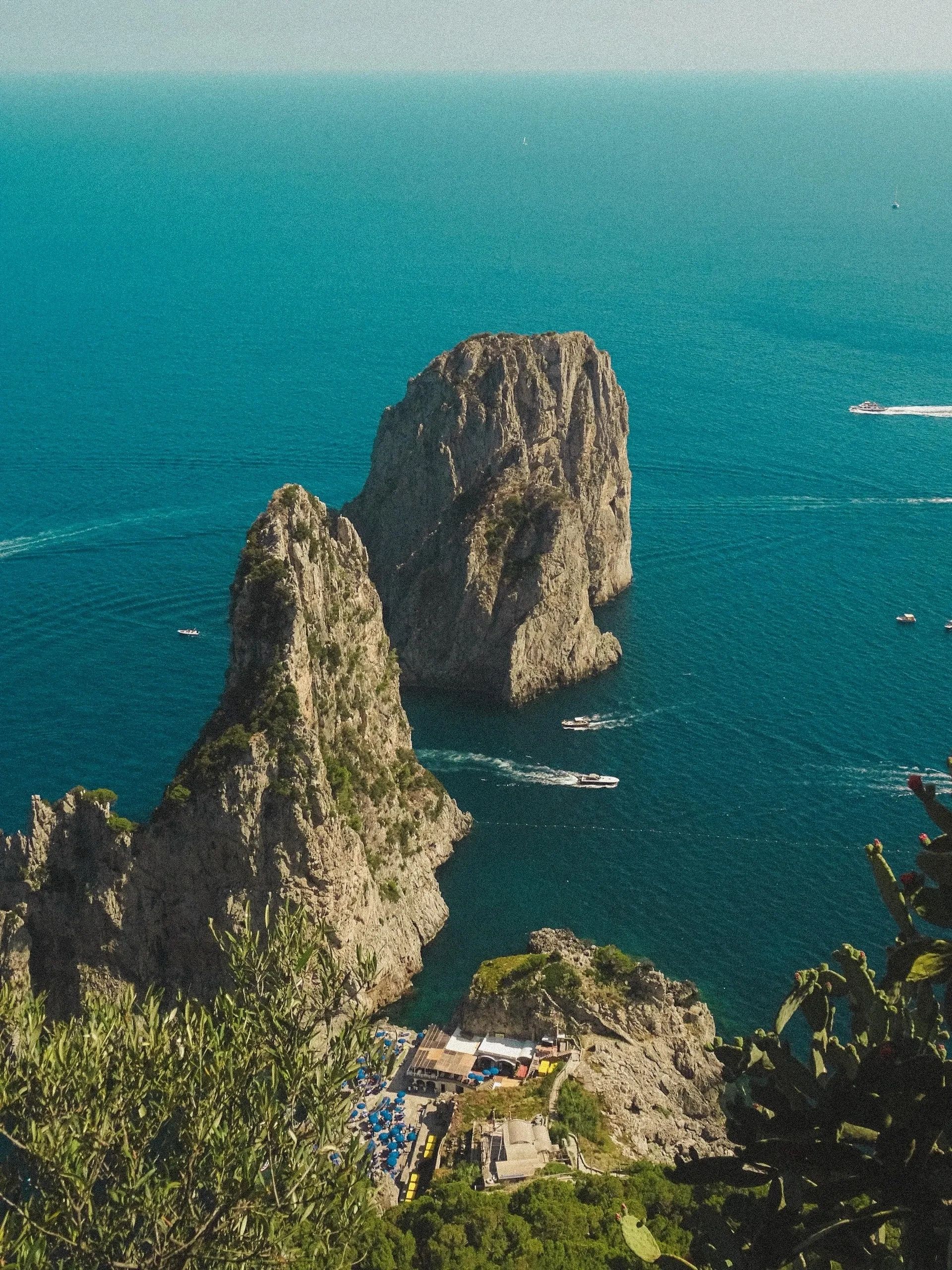 Scogliere e mare turchese a Capri con barche in movimento.
