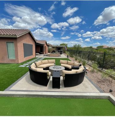 OUTDOOR SEATING AREA WITH CUSTOM FIREPIT PATIO AREA LANDSCAPED WITH PLANTS AND SYNTHETIC TURF. 