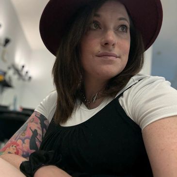 Woman with a hat and tattoo, looking thoughtfully away.