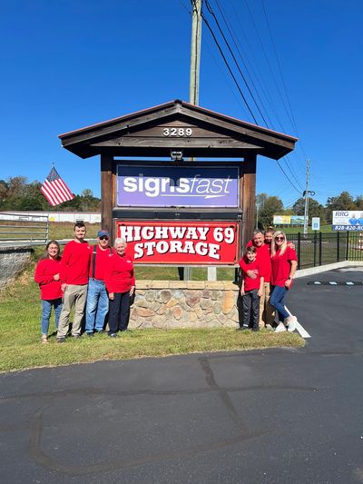 Group in red shirts standing by Highway 69 Storage sign on a sunny day.