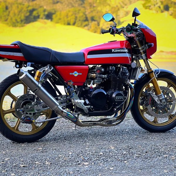 A classic red Kawasaki motorcycle with gold wheels parked on a gravel road.