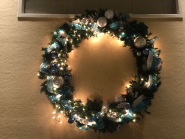 Illuminated Christmas wreath with blue and silver decorations on wall.