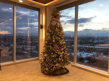 Decorated Christmas tree with cityscape view through large windows at dusk.