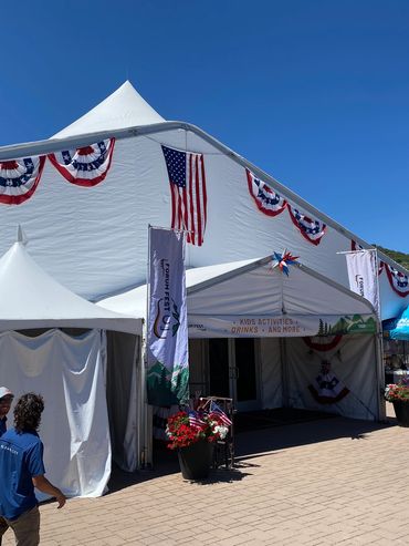 Large white festival tents decorated with American flags under a clear blue sky.