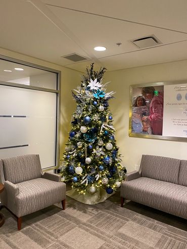 A decorated Christmas tree with blue and white ornaments in a cozy waiting area.