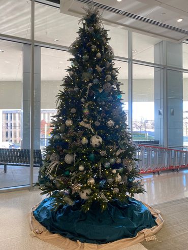 Tall Christmas tree decorated with blue, silver, and white ornaments indoors.