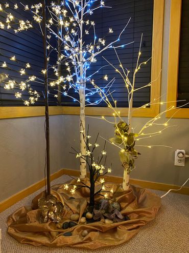 Decorative corner with illuminated artificial trees and flowers on a golden cloth.