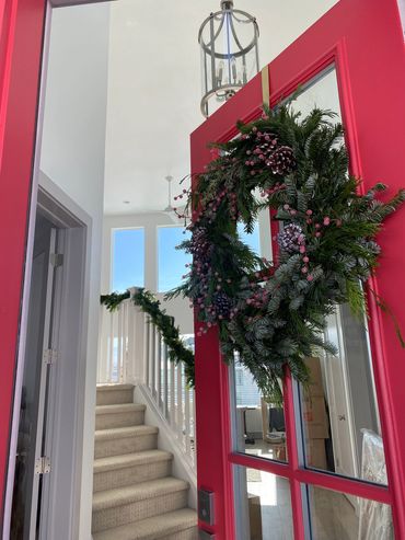 Festive wreath on a red door with decorated staircase inside.