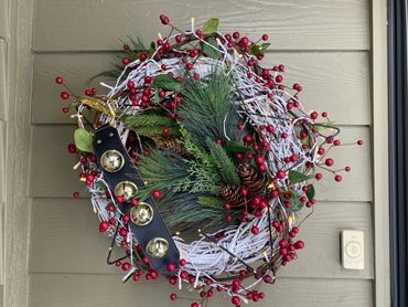 Festive wreath with red berries, pinecones, and golden jingle bells on a snowy vine base.