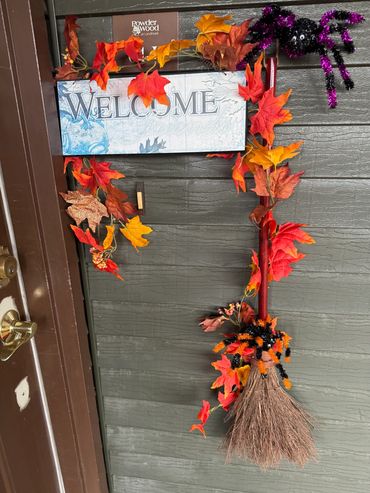Welcome sign decorated with autumn leaves, a broom, and a Halloween spider.