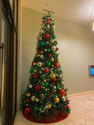 Tall Christmas tree decorated with red, green, gold, and silver ornaments and white lights.