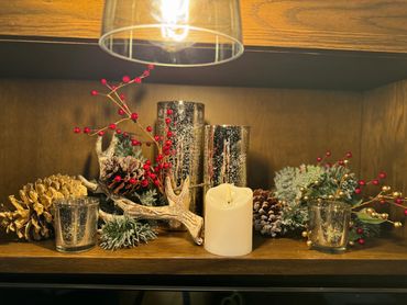 Festive holiday decor with candles, pinecones, and red berries on a wooden shelf.