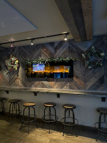 Industrial-style bar stools under a wooden counter with holiday wreaths and garland.