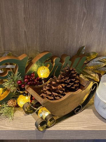 Festive holiday decor with pinecones, lights, and a wooden sleigh on a shelf.