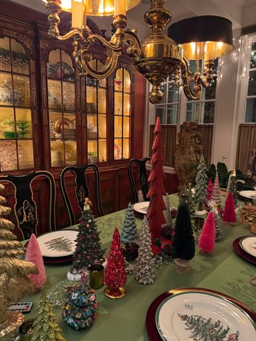Festive dining table decorated with various miniature Christmas trees under warm chandelier light.