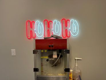 Neon Ho Ho Ho sign above a popcorn machine with a popcorn scoop.