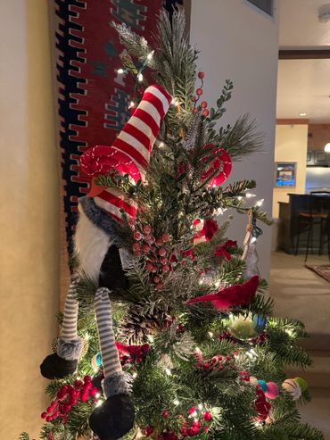 Christmas tree decorated with lights, red berries, and a striped elf figure.