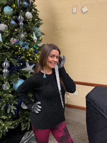 Woman smiling near a decorated Christmas tree holding a large icicle ornament.