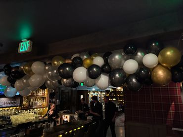 Black, white, and gold balloons decorate a dimly lit bar.