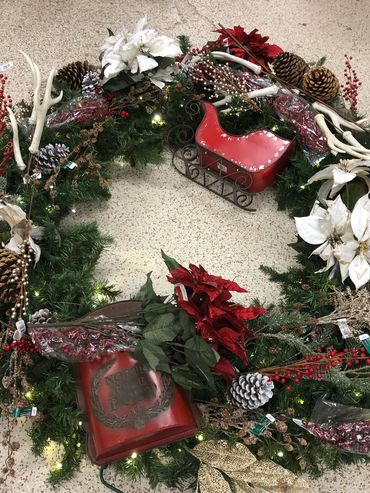 Decorative Christmas wreath with pinecones, poinsettias, and festive ornaments including a red sleigh.
